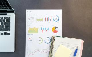 Laptop, a paper with charts, a pen and a notebook