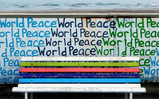 Bench in front of a wall covered with graffiti reading 'world peace'
