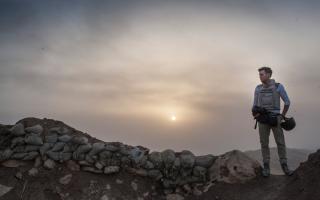 Journalist standing at the top of a mountain with a sunset in the background