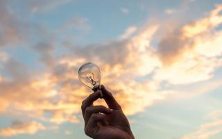 Hand holding lightbulb against the sky